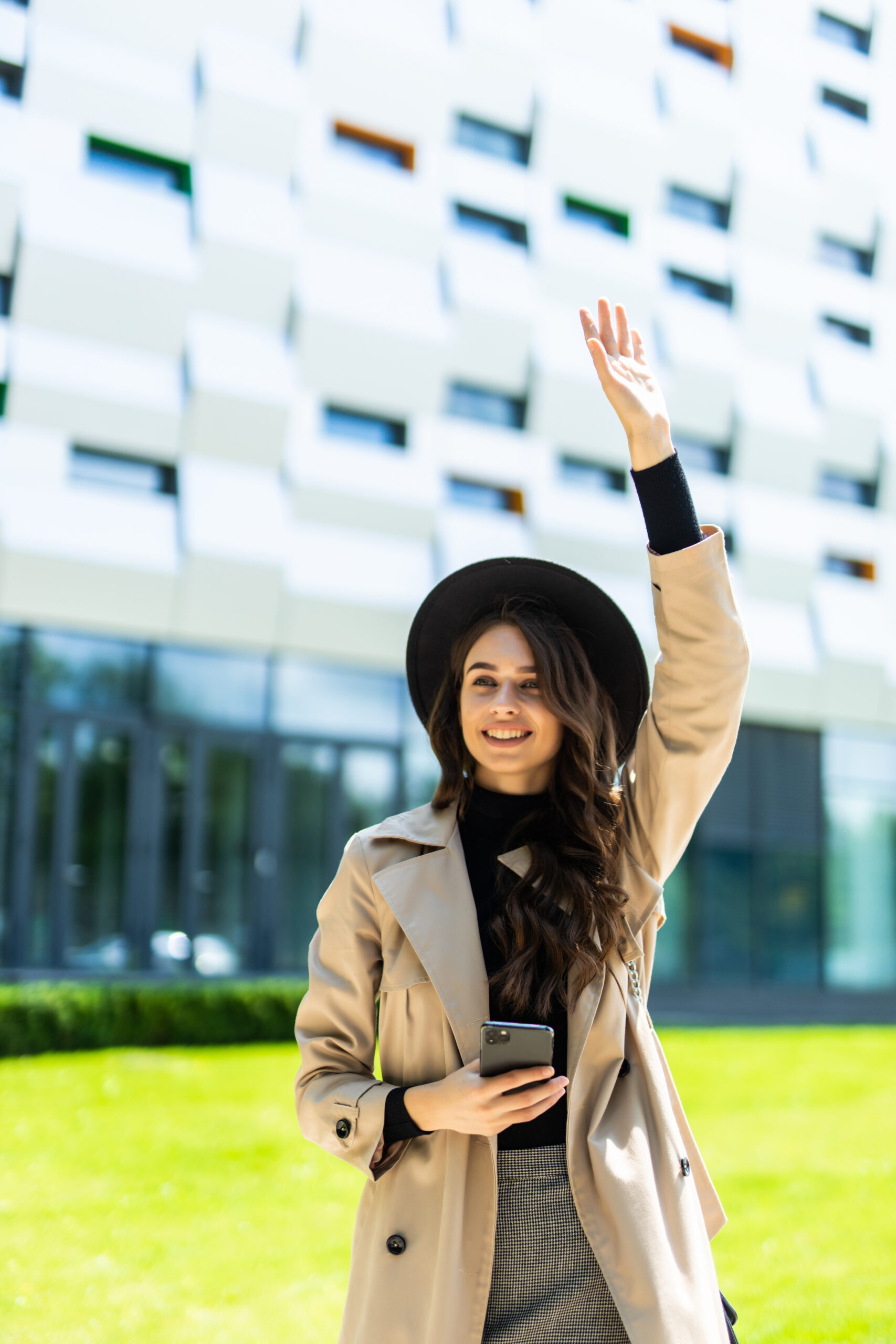 Graceful woman in coat walking down the street with phone in hand.
