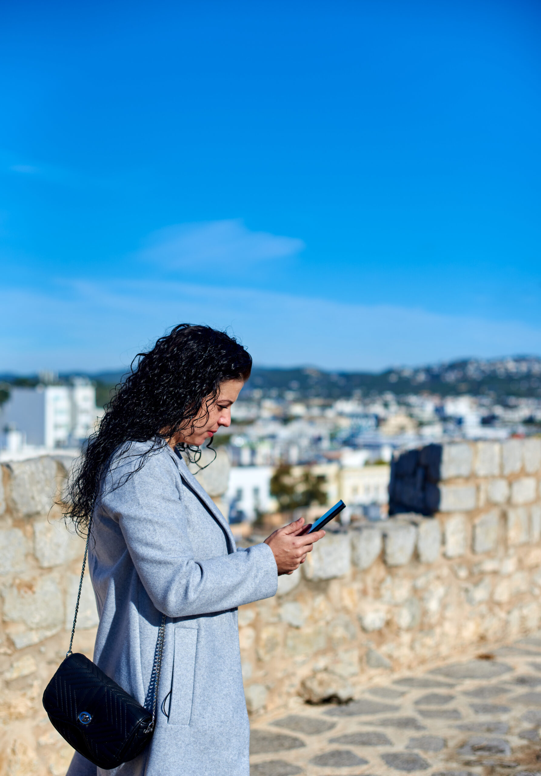 A vertical shallow focus shot of a Hispanic female sitting using her phone outdoors